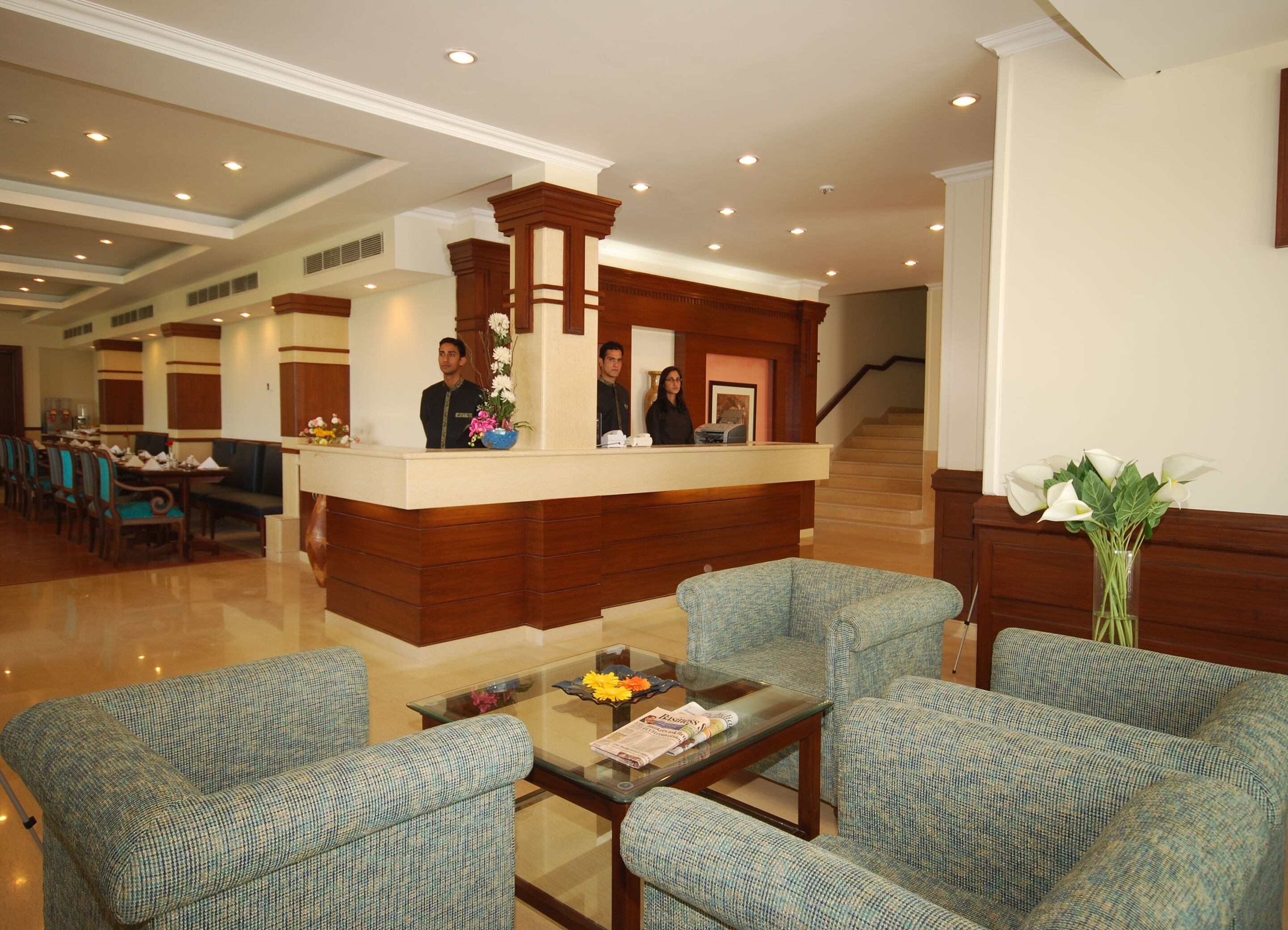 A hotel lobby with a reception desk, seating area, and a staircase.