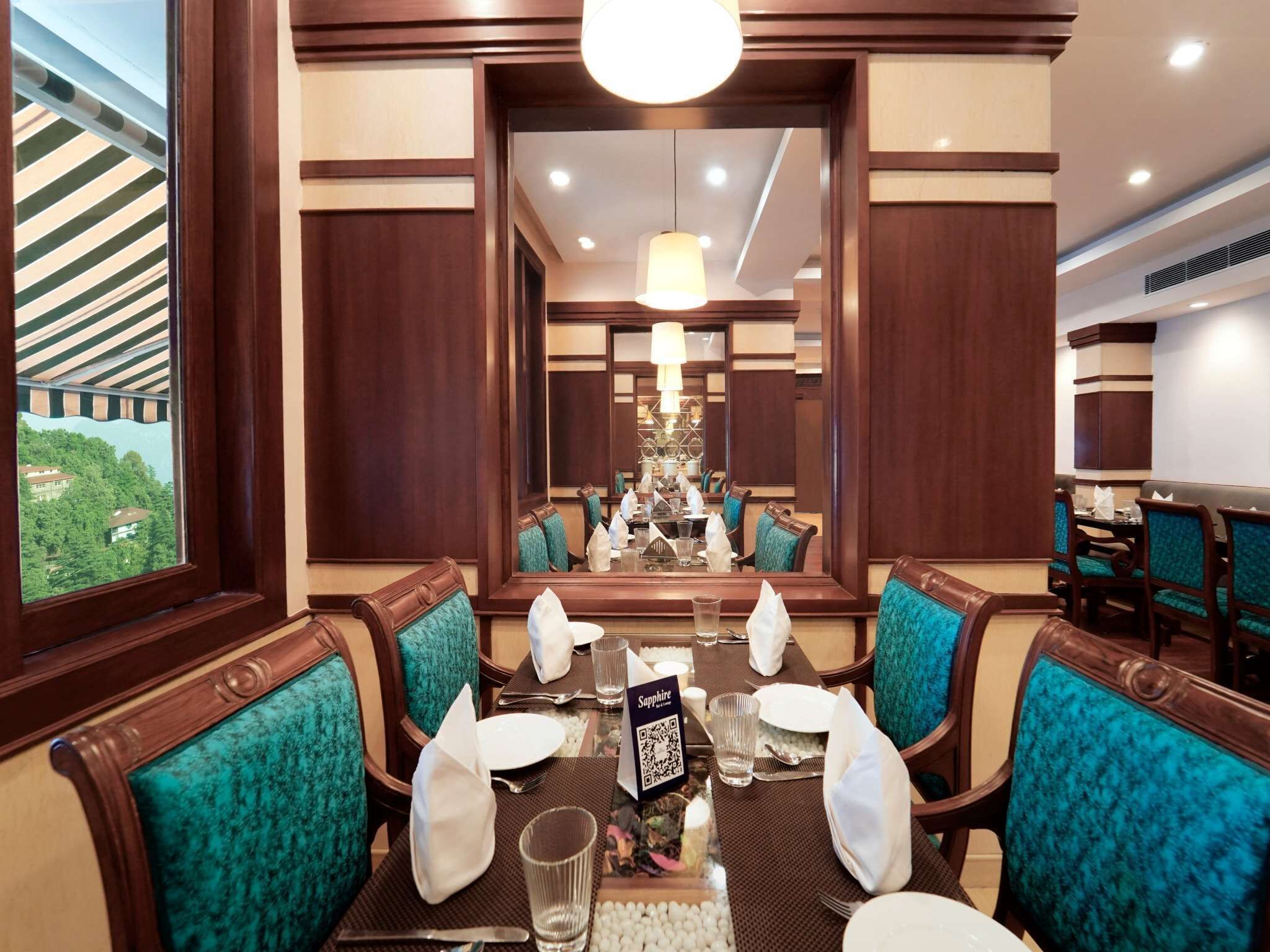 A dining area with a large mirror, teal upholstered chairs, and a table set for four.