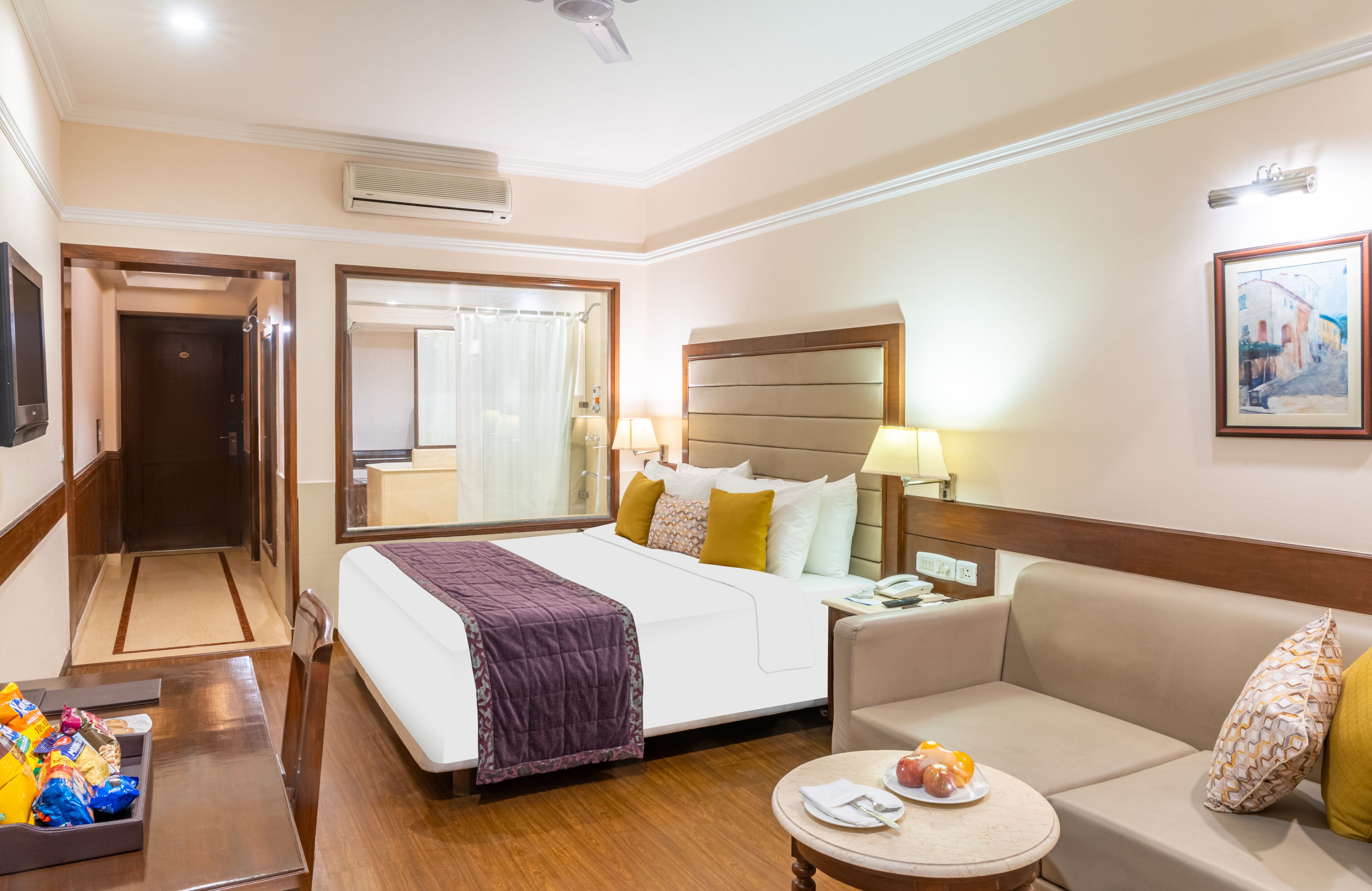 Una camera d'albergo con un letto, un divano, un tavolino con degli snack, una TV e un quadro appeso al muro.