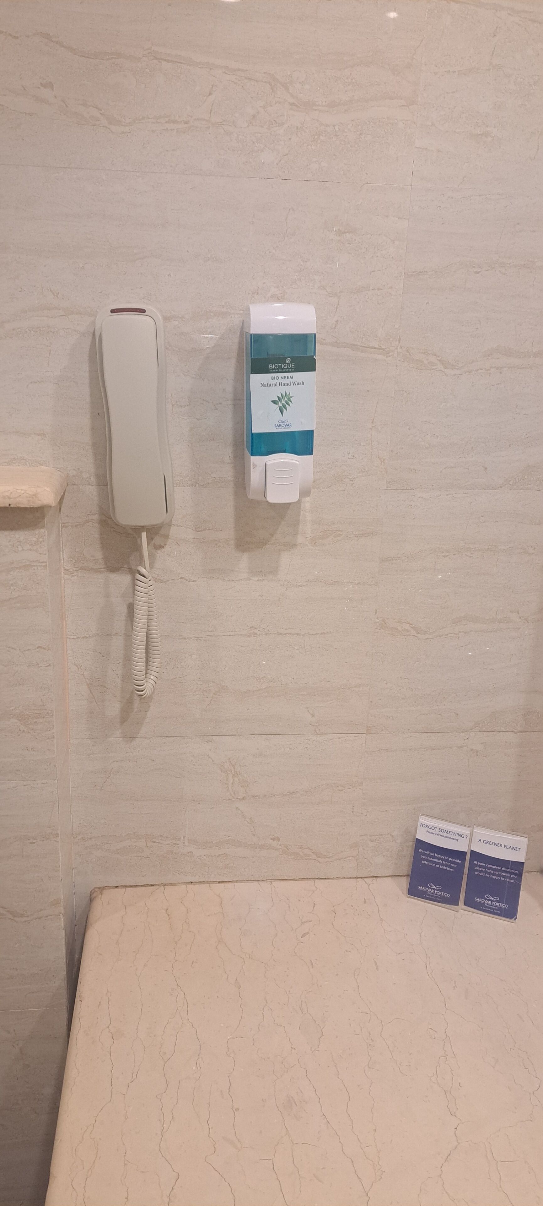 Un teléfono de pared, un dispensador de gel antibacterial y dos tarjetas informativas.