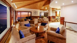 A spacious lounge area with multiple sofas and armchairs, a pool table, and a view of the sunset through large windows.