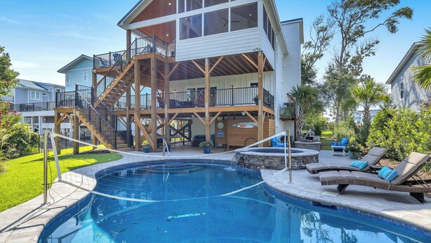 Una casa a due piani con un'ampia terrazza, una piscina e mobili da giardino.