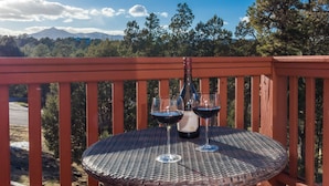 A round table with a bottle and two glasses of red wine on a balcony with a view of trees and mountains.