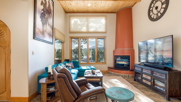 A spacious living room with a leather sofa, a television, a fireplace, and large windows.