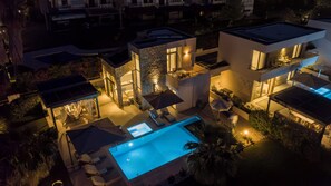 Une maison moderne dotée d’une piscine, d’un espace salon extérieur et d’une terrasse bien éclairée.