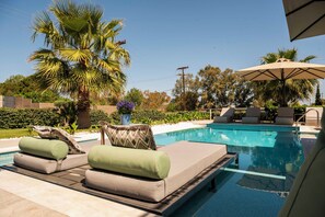 Un espace piscine avec des chaises longues, un palmier et un ciel d’un bleu éclatant.