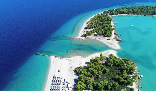 An aerial view of a coastal area with a sandy beach, clear turquoise waters, and a densely forested island.