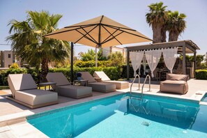 Un área de piscina con sillones, una pérgola con toldo y una mesa junto a la piscina.