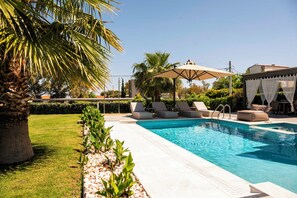 Ein Pool mit Liegestühlen und Sonnenschirmen, umgeben von Grünpflanzen und einem Steingarten.