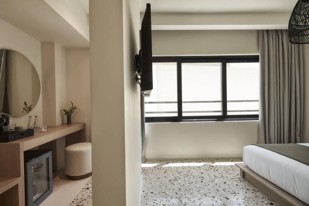 Camera d'albergo moderna con un letto, una TV a parete, un piccolo angolo salotto e una finestra con tende.