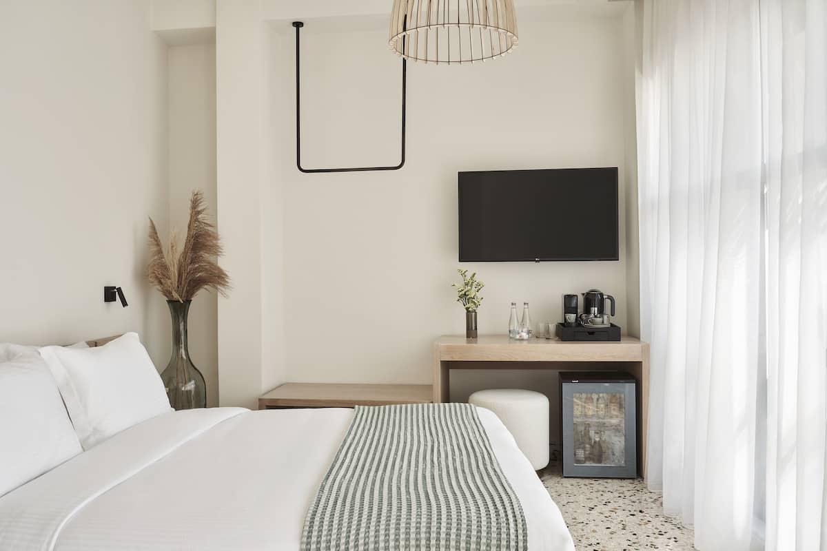 Una camera d'albergo moderna con un letto grande, una scrivania con TV a schermo piatto, una macchina del caffè e un piccolo frigorifero.