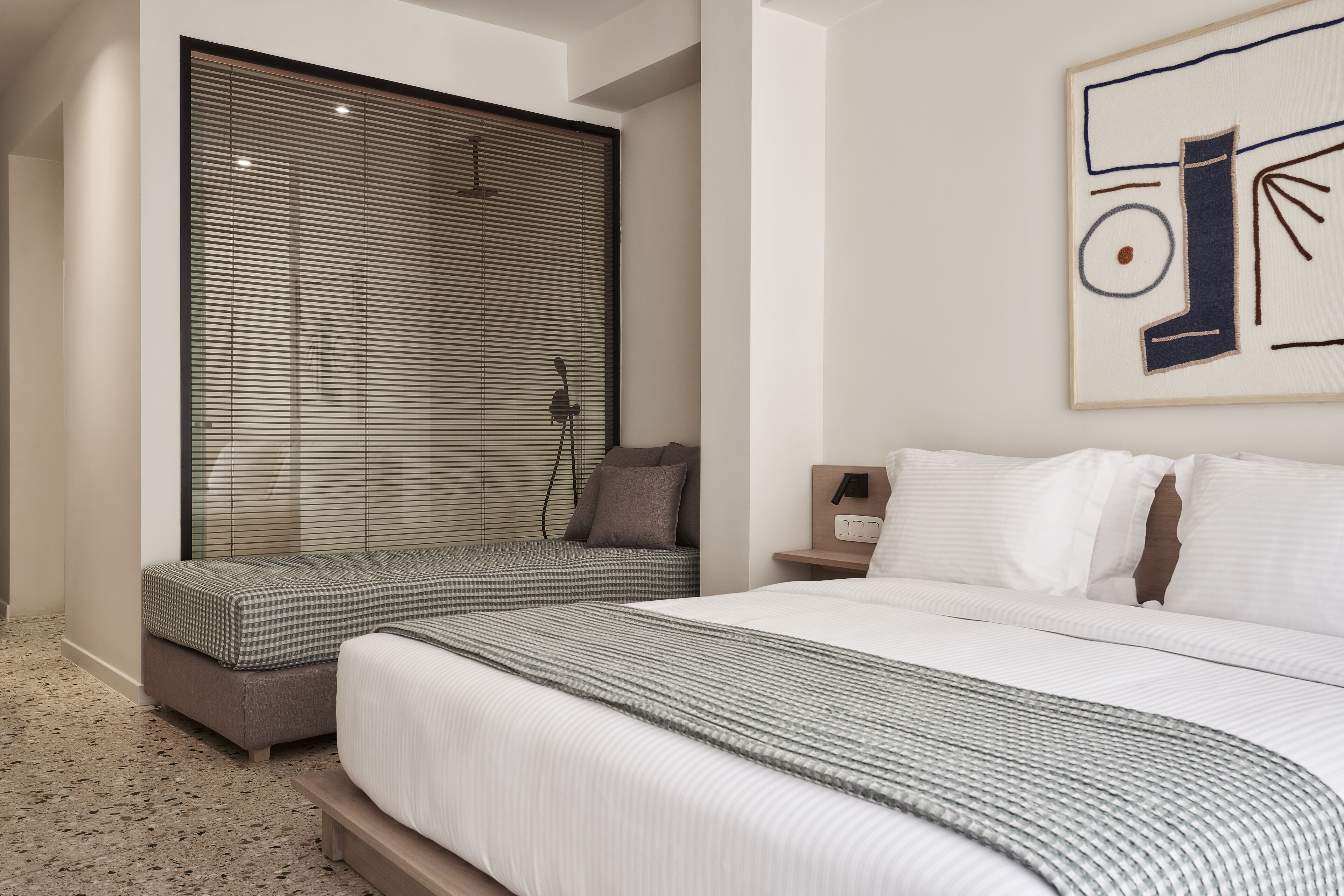 Quarto com duas camas, uma janela grande com cortinas, uma obra de arte na parede e uma mesa de cabeceira com abajur.