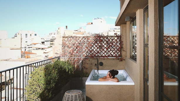Un balcón con un jacuzzi, un taburete de mimbre y vistas a la ciudad.