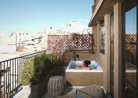 Uma varanda com banheira de hidromassagem, um banquinho de vime e vista para a paisagem urbana.