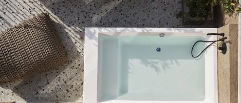 A rectangular bathtub with a faucet and a control knob, placed on a terrazzo floor with a textured cushion beside it.