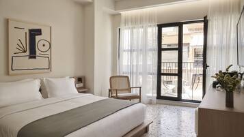 A hotel room with a large bed, a chair, a desk, and a balcony with a view.