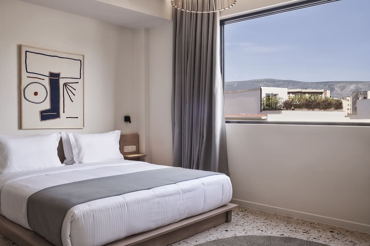 Una camera d'hotel moderna con un letto grande, vista sulla città e un'opera d'arte astratta appesa al muro.
