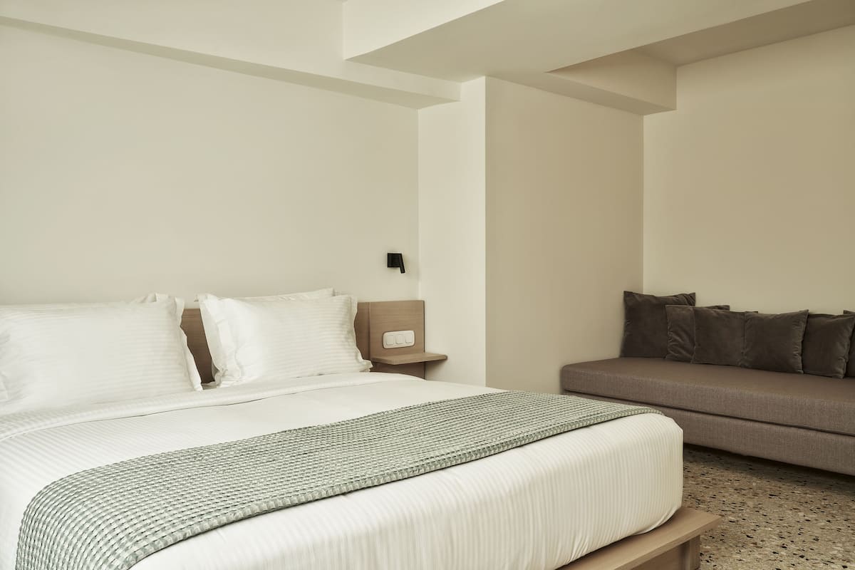 Una camera d'albergo con un letto, un comodino, un divano e un pavimento rivestito di moquette.