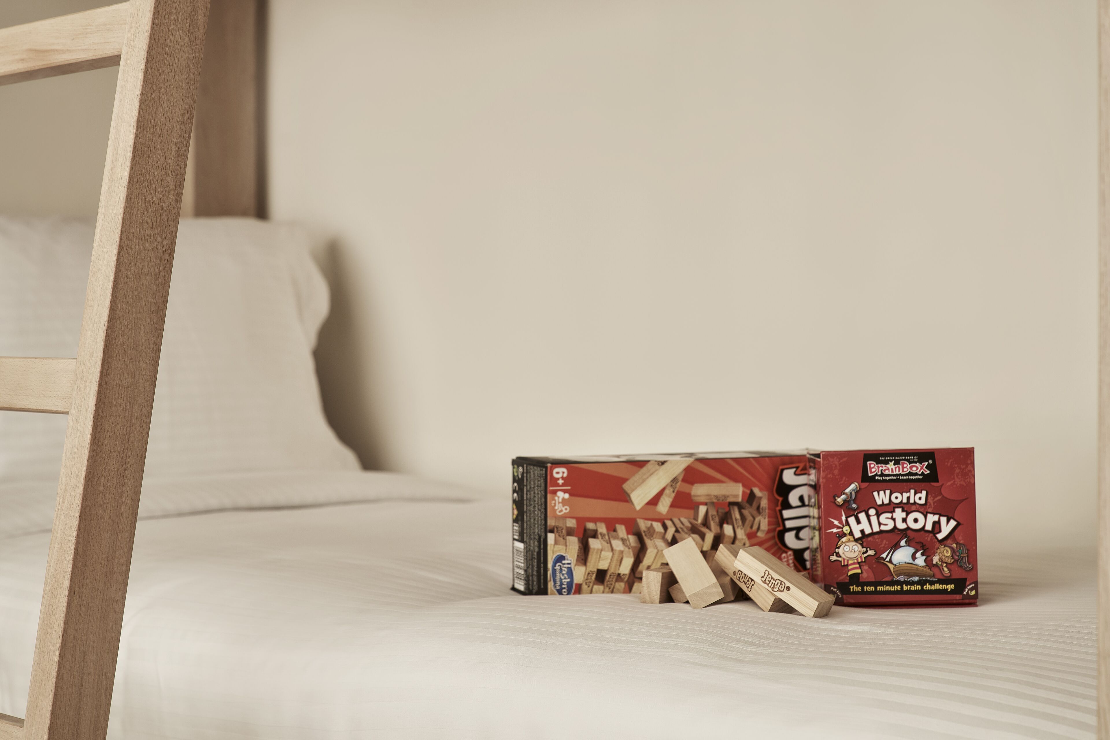 A wooden bed frame and a box of 'BrainBox World History' puzzles on a bed.