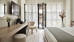 Una habitación de hotel con cama, escritorio con silla, espejo grande y vistas al exterior a través de una puerta de cristal.