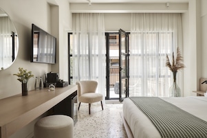 Quarto de hotel com cama, escrivaninha com cadeira, espelho grande e vista para o exterior através de uma porta de vidro.