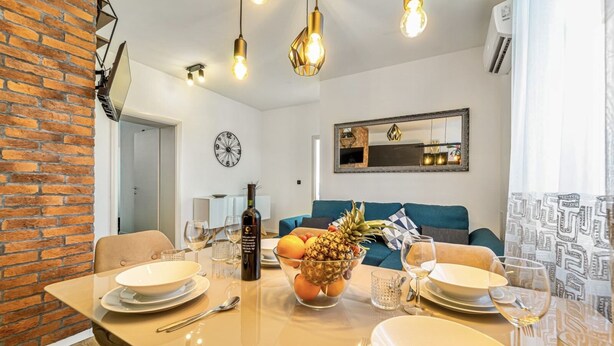 A dining area with a table set for two, a bowl of fruit, and a bottle of wine. There is a sofa and a mirror in the background. - 4*Flat in the Heart of the City, Onsite parking, Wifi (Split)