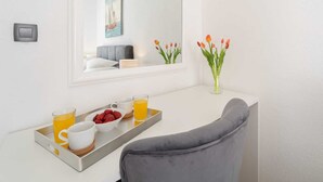 A modern hotel room with a white desk, a grey chair, a tray with breakfast items, a vase with flowers, and a painting of a sailboat. - 4*Flat in the Heart of the City, Onsite parking, Wifi (Split)