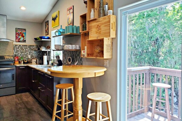 A kitchen with wooden bar stools, a large window, and a balcony with a wooden railing.