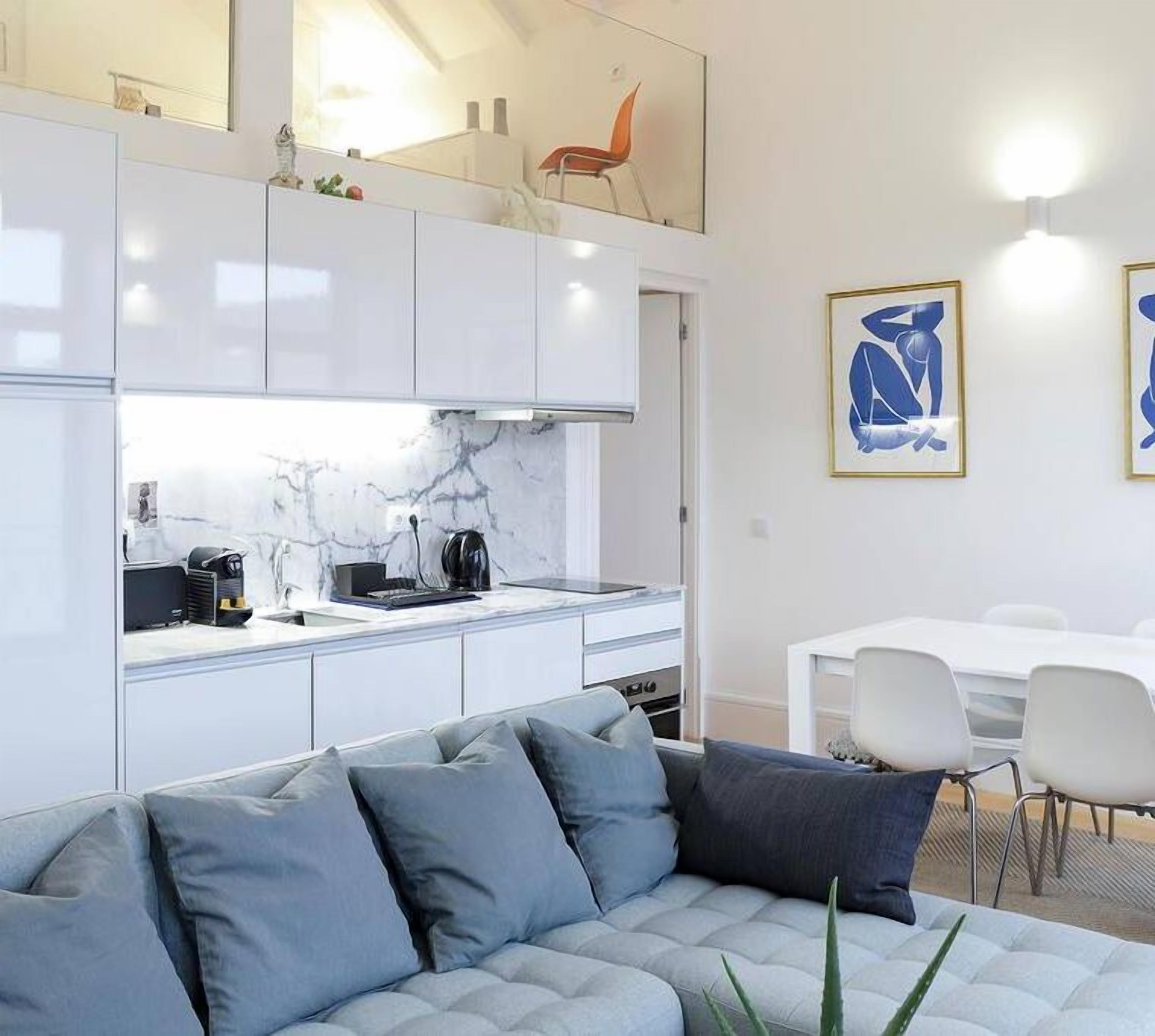 A modern kitchen with white cabinets, a marble backsplash, and a dining area with a white table and chairs.