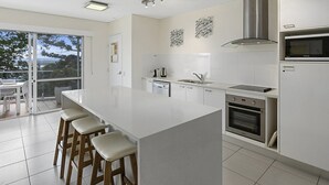 Eine moderne Küche mit einer großen Kochinsel, Edelstahlgeräten und einer Glastür zum Balkon.
