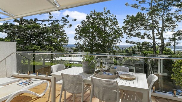 Ein Balkon mit Tisch und Stühlen, einer Topfpflanze und Blick auf Bäume und das Meer.
