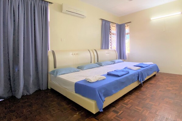 Habitación individual con piso de madera, cama con ropa de cama azul y blanca y ventana con cortinas.
