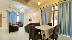 A dining area with a table set for four, surrounded by chairs, and a sofa in the background.