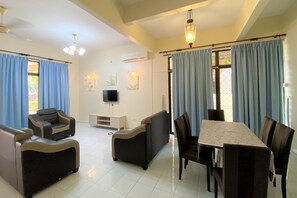 A spacious living area with a sofa set, a dining table, and chairs. There is a flat-screen TV mounted on the wall, and the room has a ceiling fan. - OYO 90199 Homely&cozy House (George Town)