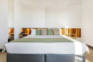 A modern hotel room with a large bed, wooden headboard, bedside tables with lamps, and a green throw blanket. - Lato Annex Boutique Rooms (Heraklion)