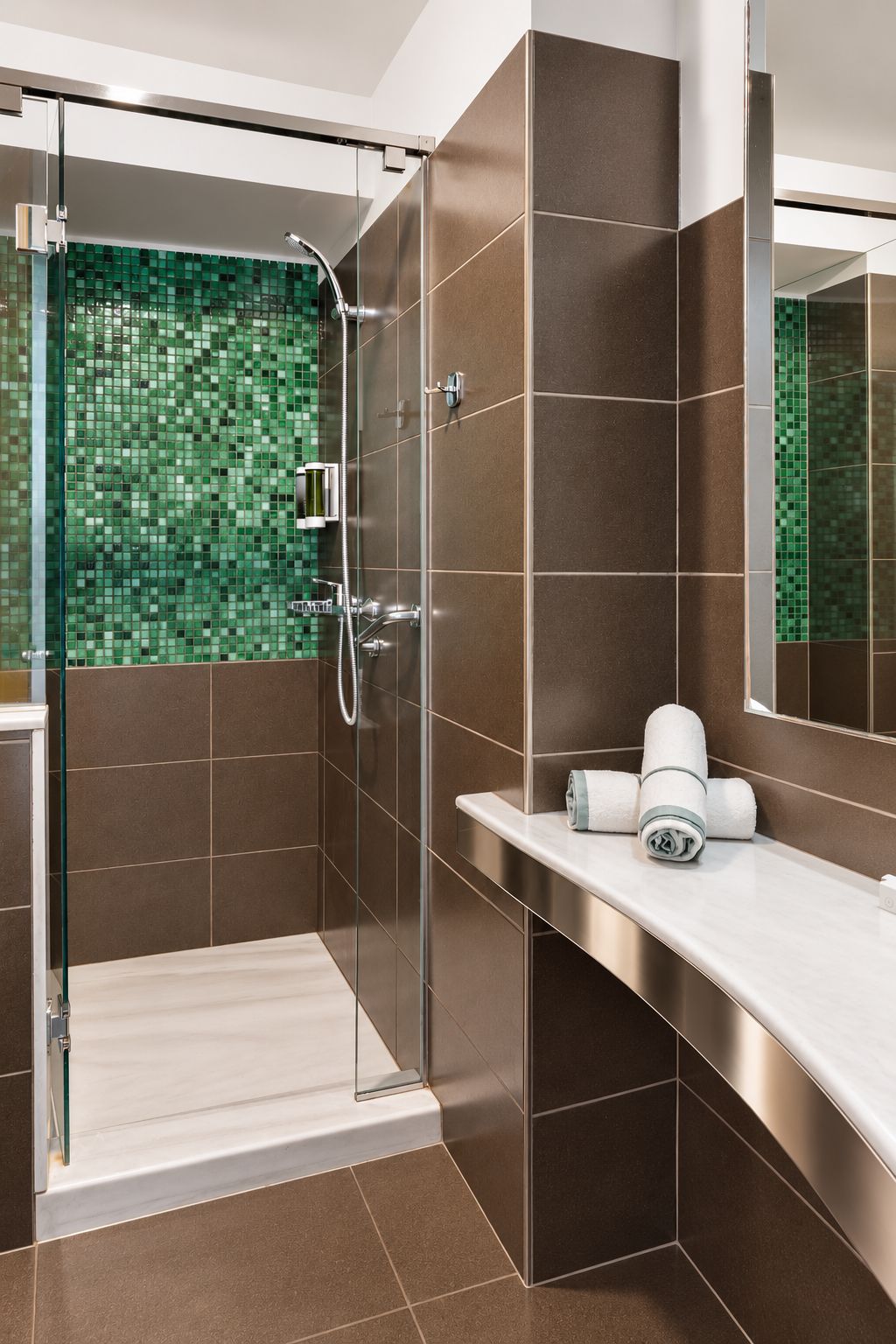 A modern bathroom with a glass shower enclosure, a white countertop, and a green mosaic tile wall.