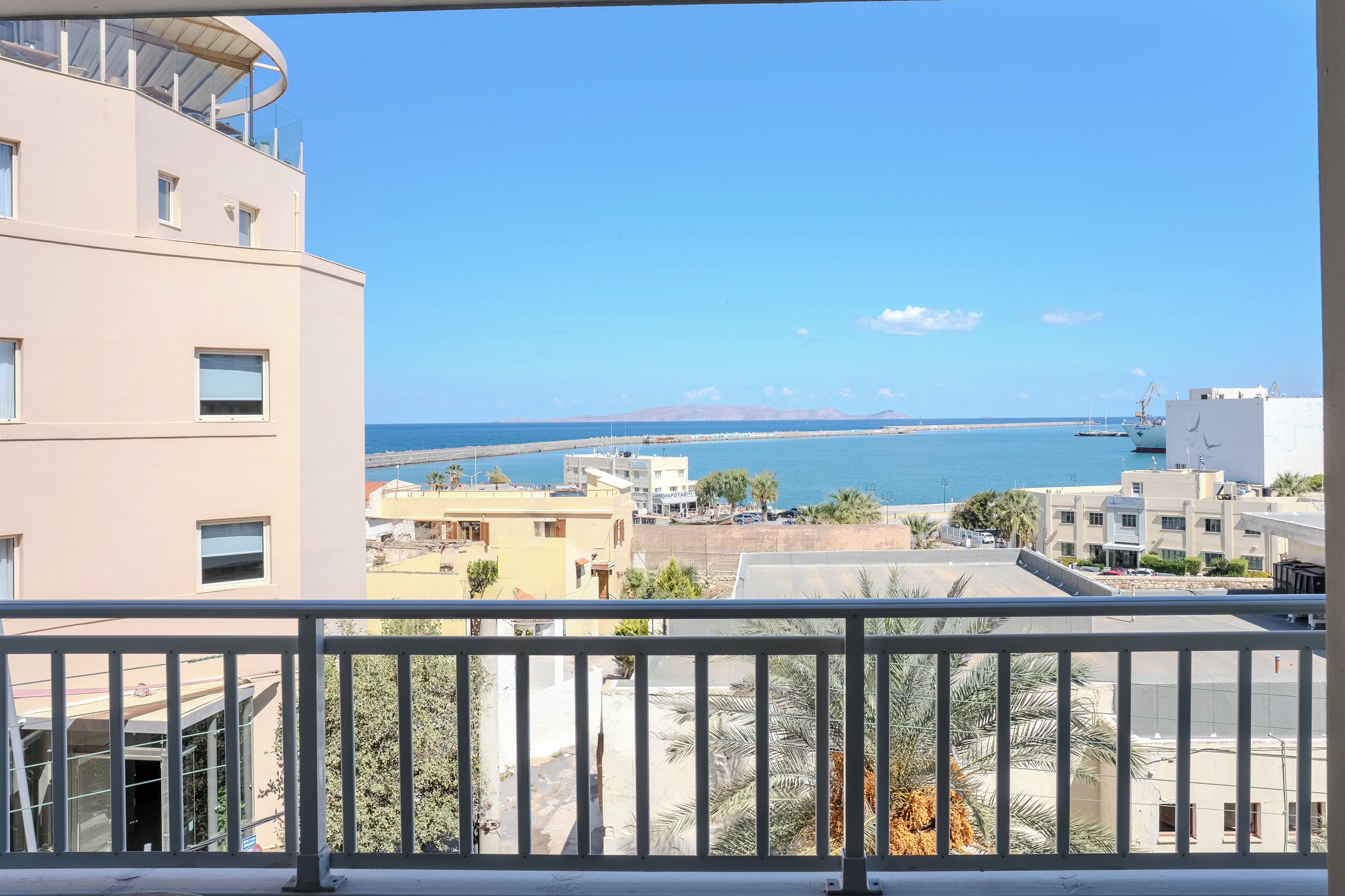 A balcony with a view of a coastal cityscape, including buildings and a clear blue sky.