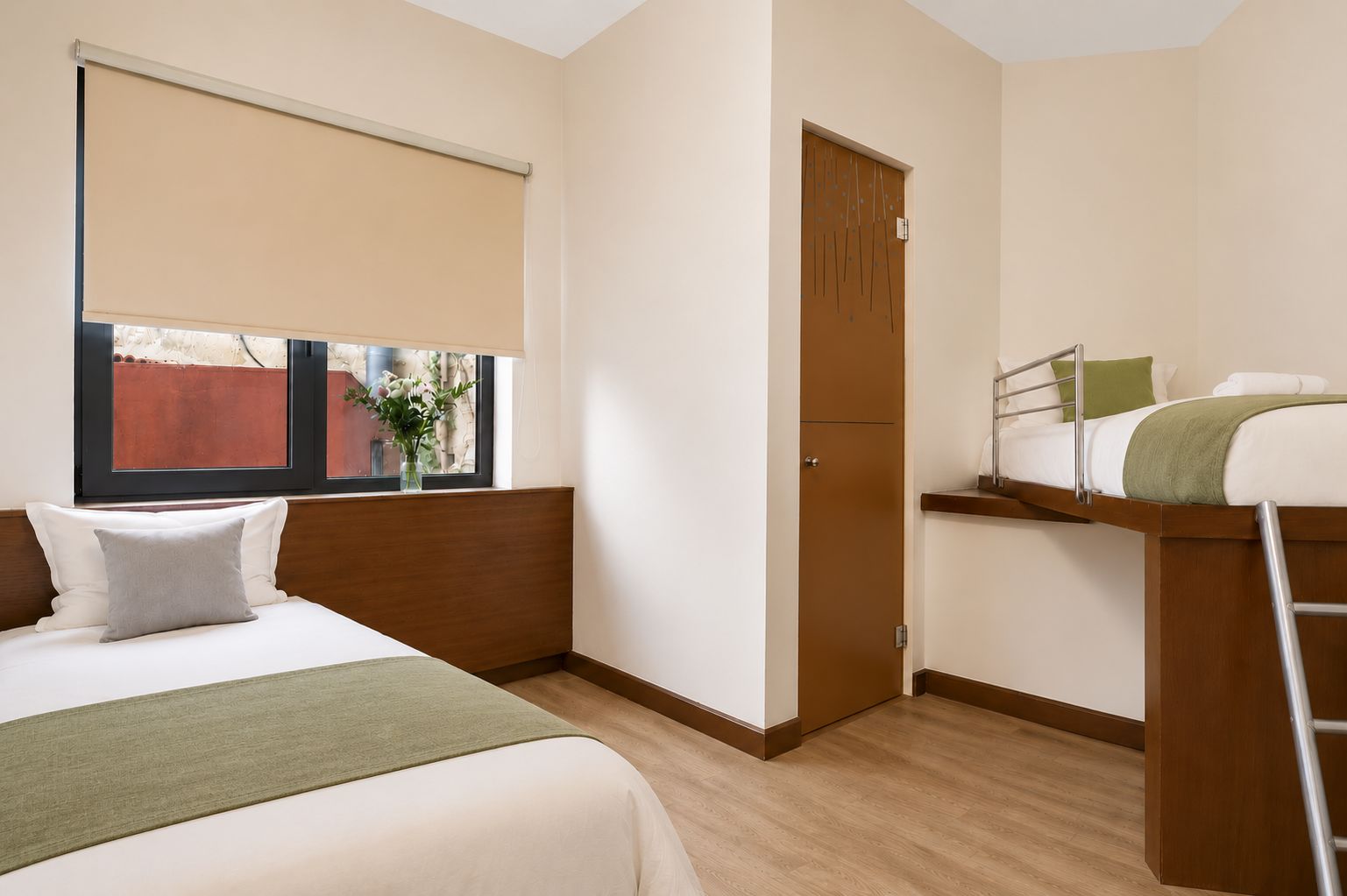 Habitación de hotel con cama, ventana con vista, puerta y una pequeña mesa con una silla.