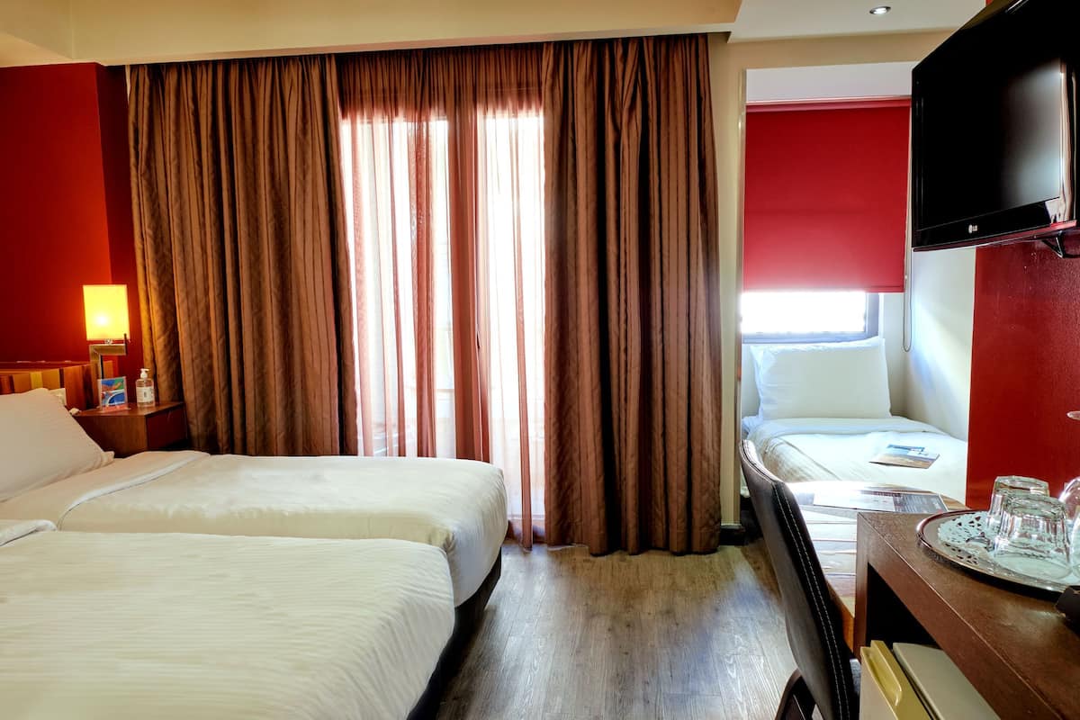 A hotel room with two beds, a television, a desk with a tray, and a window with curtains.