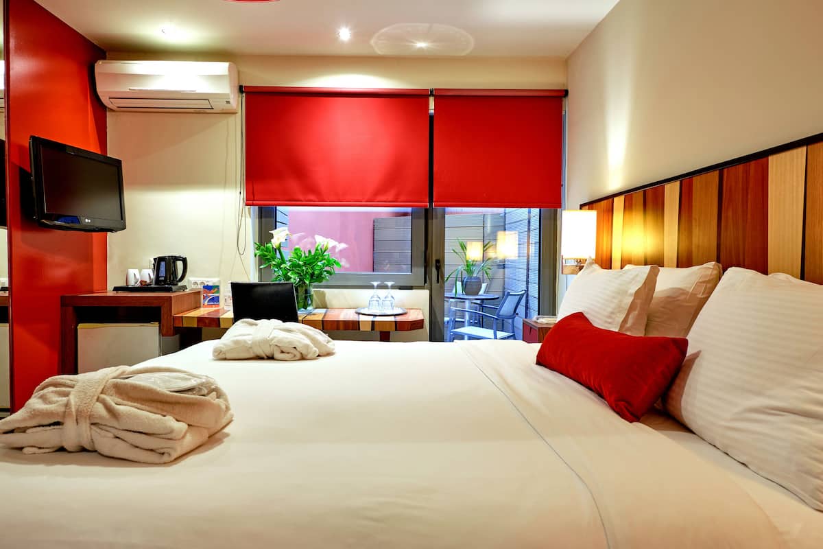 A hotel room with a bed, a desk, a chair, a TV, and a window with red curtains.