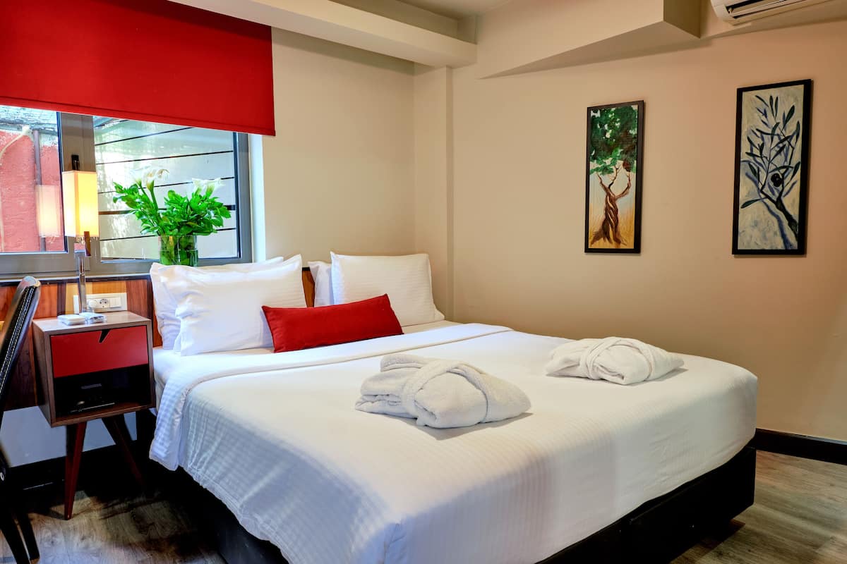 A hotel room with a bed, a desk, a lamp, a potted plant, and two paintings on the wall.