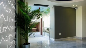 A modern lobby with a large potted plant, a glass wall with white text, and a curved ceiling. - Lato Annex Boutique Rooms (Heraklion)
