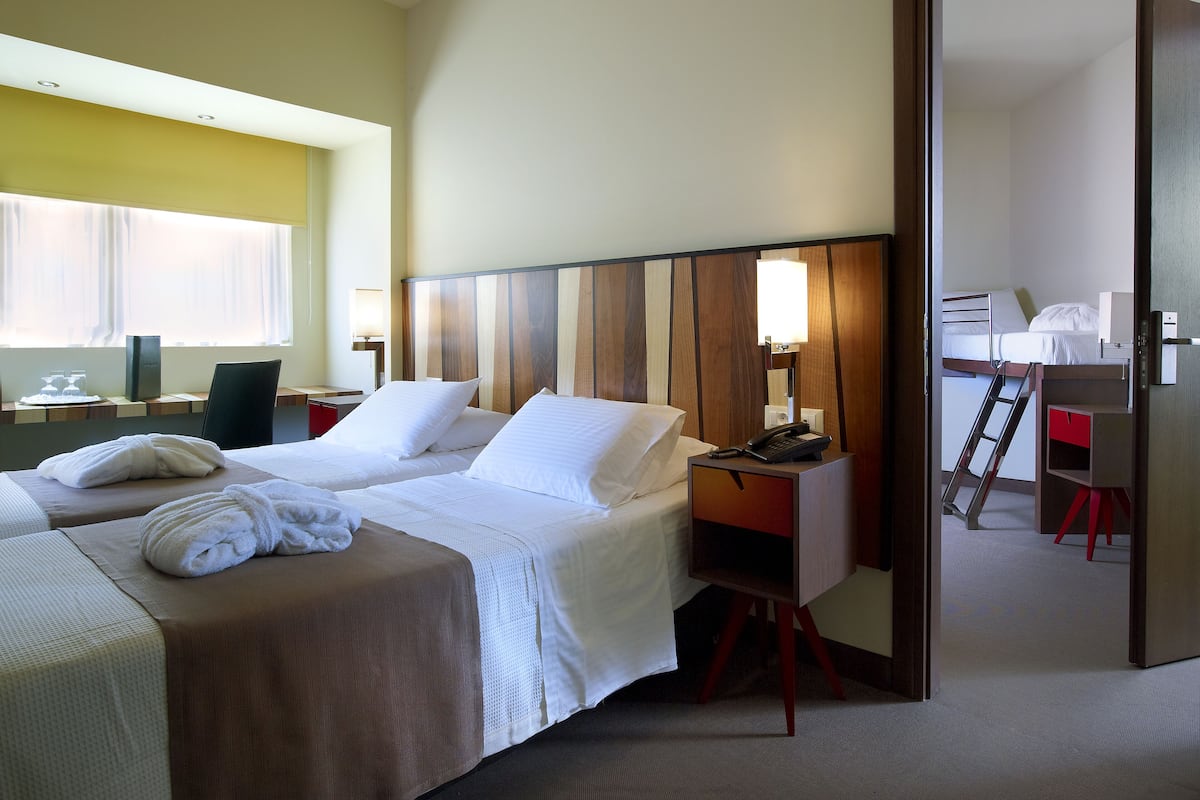 A hotel room with two beds, a desk, a chair, and a bathroom visible through an open door.