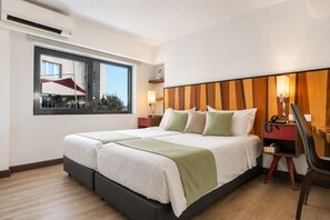 A hotel room with a bed, bedside table, lamp, chair, and a window with a view of the outside.