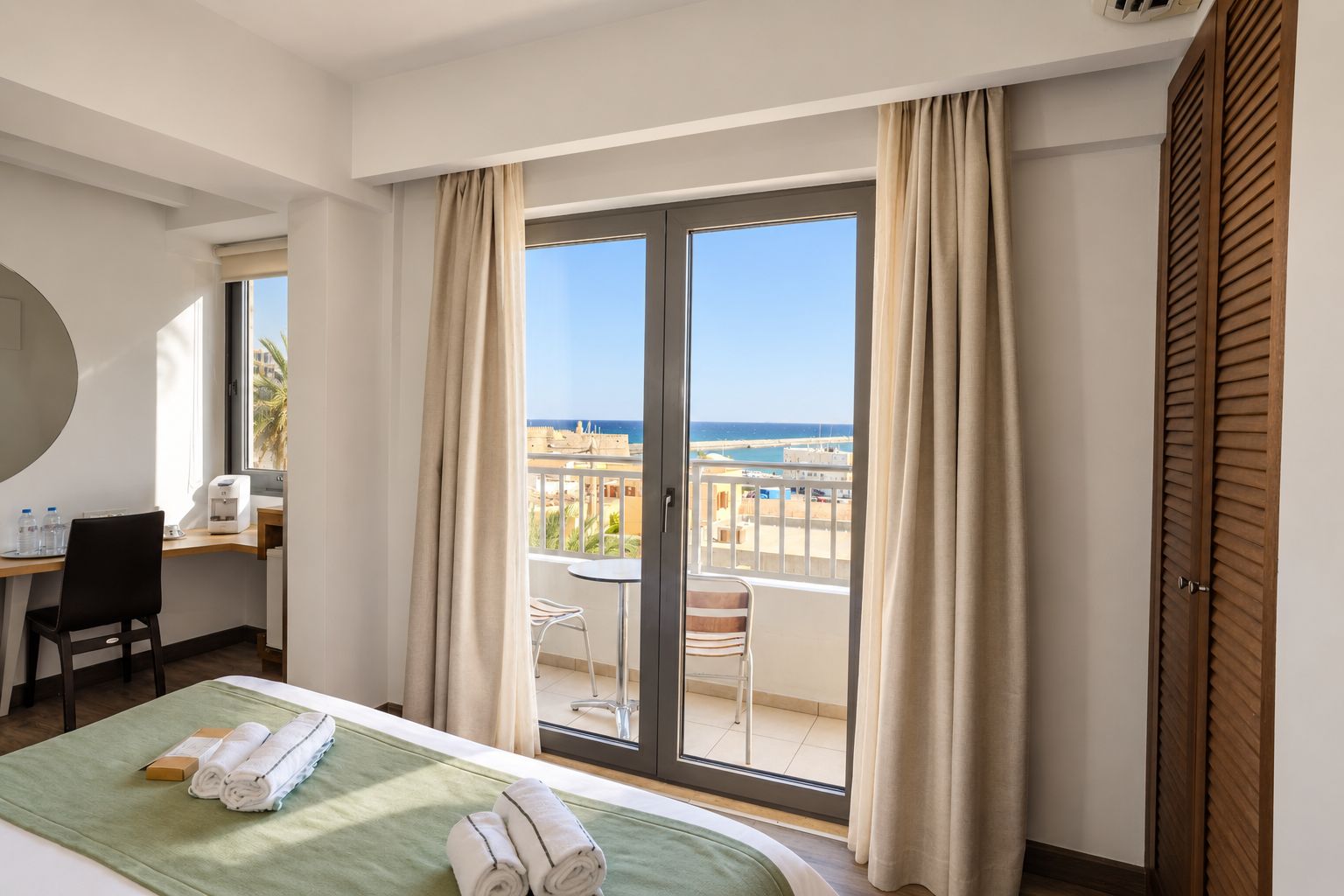 Une chambre d’hôtel avec un lit, un bureau, une chaise, une table et une vue sur la mer.