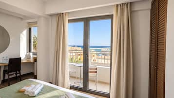 A hotel room with a bed, a desk, a chair, a table, and a view of the sea.