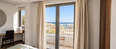 Een hotelkamer met een bed, bureau, stoel, tafel en uitzicht op zee.