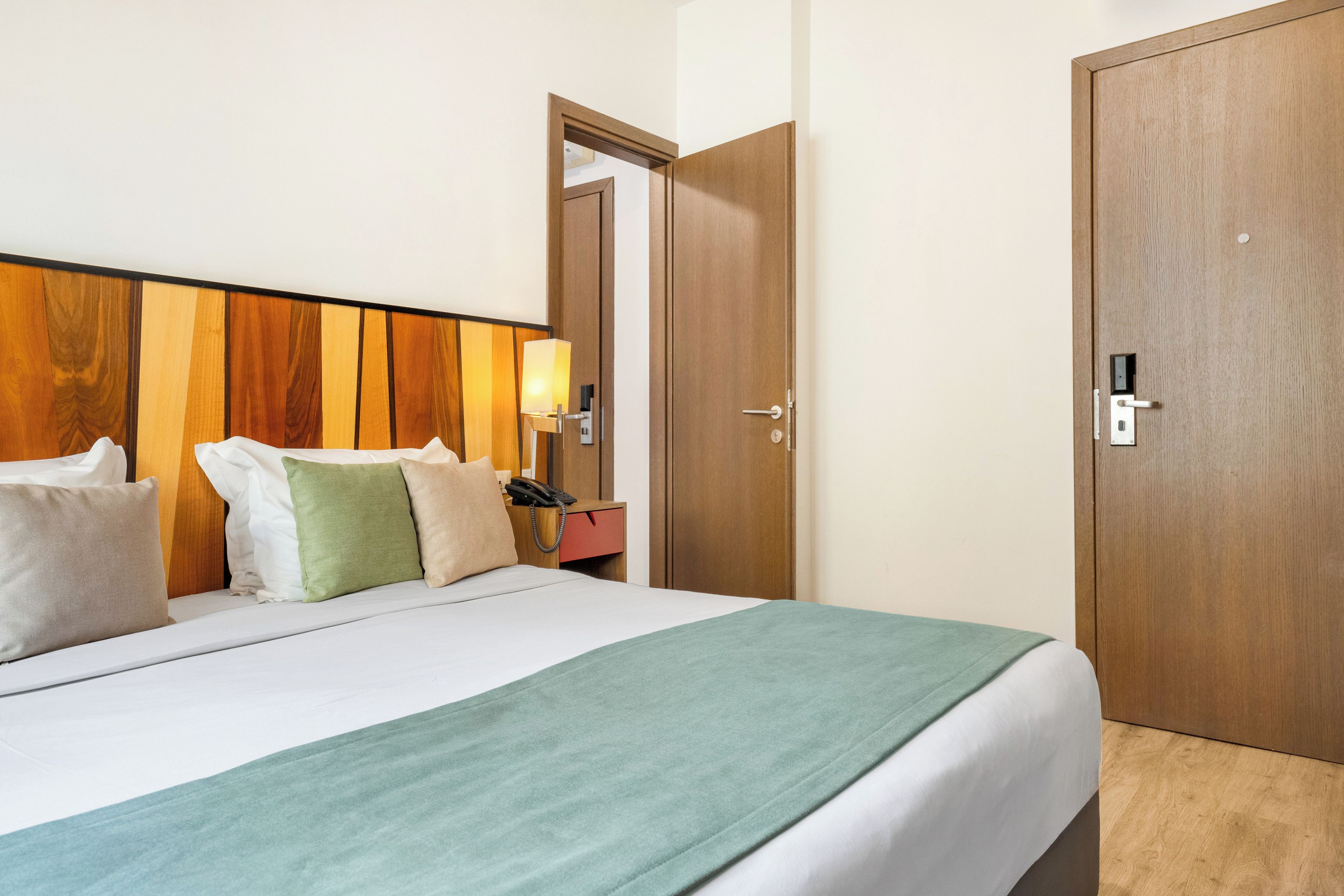 Una habitación de hotel con cama, mesita de noche, lámpara y un armario de madera.