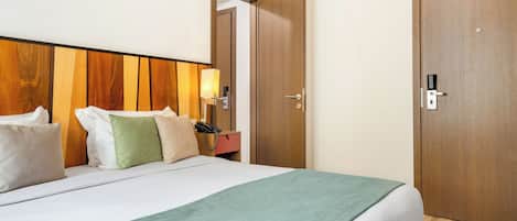 Una habitación de hotel con cama, mesita de noche, lámpara y un armario de madera.