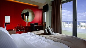 A hotel room with a large bed, a desk with a chair, a TV, and a view of the city. - Lato Annex Boutique Rooms (Heraklion)